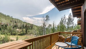 Un terrazzo in legno con vista su un pendio boscoso. Si notano due poltrone in vimini e un tavolino rotondo.
