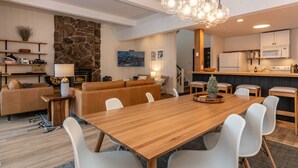 Un'ampia zona giorno con un tavolo da pranzo in legno, sedie bianche, un divano e un angolo cottura con mobili ed elettrodomestici bianchi.