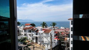 Une vue sur la ville côtière, avec ses bâtiments blancs et ses toits recouverts de tuiles rouges, prise depuis une fenêtre donnant sur la mer.
