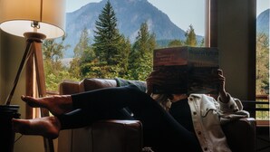 Una persona reclinada en una silla junto a una ventana con vistas a montañas.