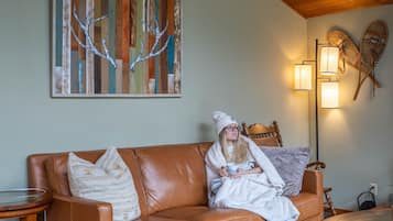 A cozy living room with a brown leather sofa, a wooden ceiling, and a wall-mounted abstract painting.