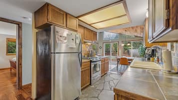 A modern kitchen with wooden cabinets, a stainless steel refrigerator, a built-in oven, and a stone tile backsplash.