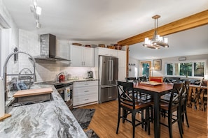 A modern kitchen with white cabinets, a stainless steel refrigerator, and a wooden dining table with chairs.