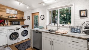 Une cuisine moderne avec des meubles blancs, un lave-linge encastré, un évier et une fenêtre donnant sur un espace verdoyant.