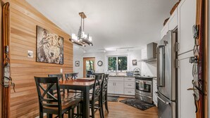 Une cuisine moderne avec un lambris en bois, des appareils en acier inoxydable et un coin repas comprenant une table et des chaises en bois.
