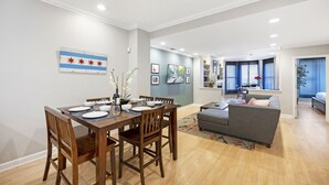 A modern living room with a dining area, featuring a wooden dining table, chairs, a grey sofa, and a colorful rug.