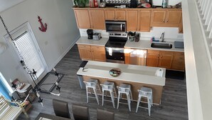 Une cuisine moderne avec des meubles en bois, un îlot central doté de tabourets, et un coin repas avec une table et des chaises.