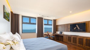 Habitación de hotel con cama, escritorio, silla, televisión y vista al mar.