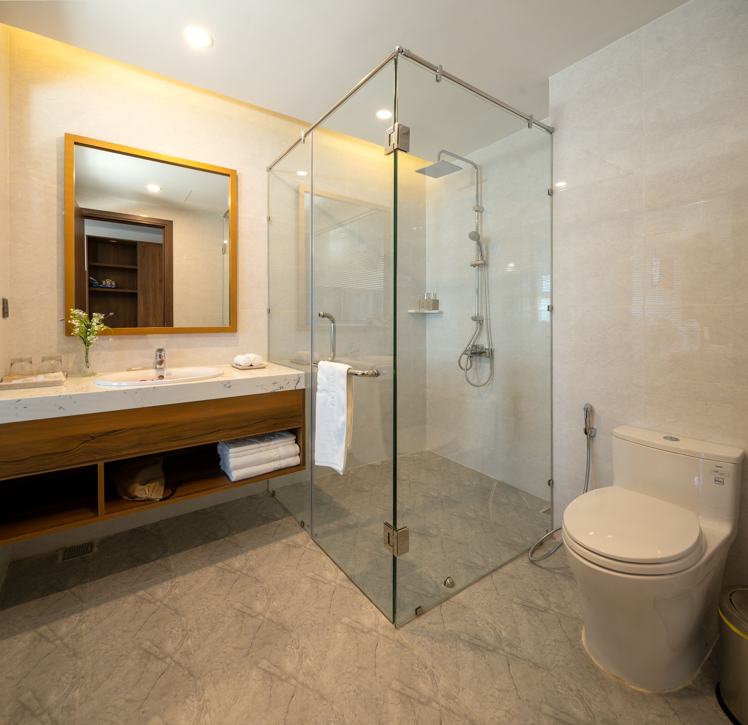 Een moderne badkamer met een douchecabine van glas, een houten wastafelmeubel, een toilet en een grote spiegel.
