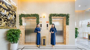 Un vestíbulo con dos recepcionistas uniformadas de azul, un cuadro decorativo grande y una planta en maceta.
