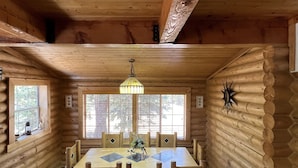 A log cabin interior with a wooden dining table, chairs, and a hanging light fixture. - Hot Tub at Our Family cabin. It’s great for all family sizes and year round fun! (Duck Creek Village)