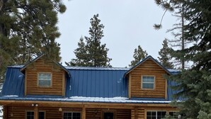 A two-story log cabin with a metal roof, surrounded by snow and pine trees. - Hot Tub at Our Family cabin. It’s great for all family sizes and year round fun! (Duck Creek Village)