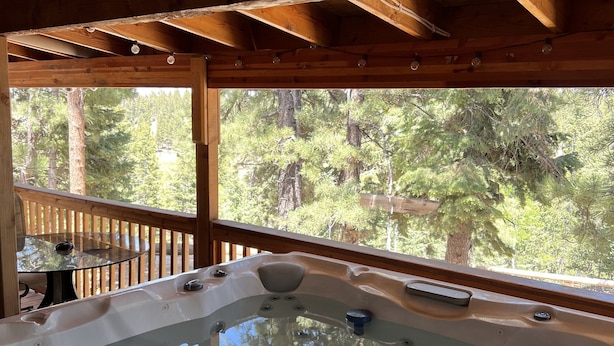 A wooden deck with a hot tub and a glass table. - Hot Tub at Our Family cabin. It’s great for all family sizes and year round fun! (Duck Creek Village)