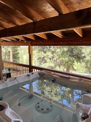 A wooden deck with a hot tub and a glass table. - Hot Tub at Our Family cabin. It’s great for all family sizes and year round fun! (Duck Creek Village)