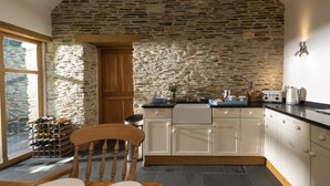 Une cuisine avec des murs en pierre, des armoires blanches, une chaise en bois et un meuble à vin.