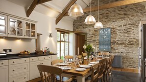 Une cuisine spacieuse avec des meubles blancs, un mur en pierre et un coin repas comprenant des chaises en bois et une table dressée pour six personnes.