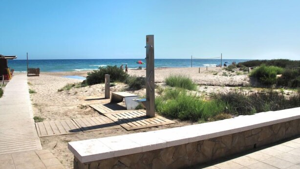 Ein Strand mit einer Holzpromenade, die zum Meer führt, einer Steinmauer und freiem Blick auf den Ozean.