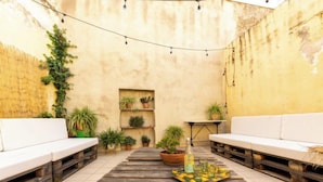 Ein gemütlicher Patio-Bereich mit zwei weißen Sofas, einem Holztisch mit Getränken auf einem Tablett und Blumentöpfen.