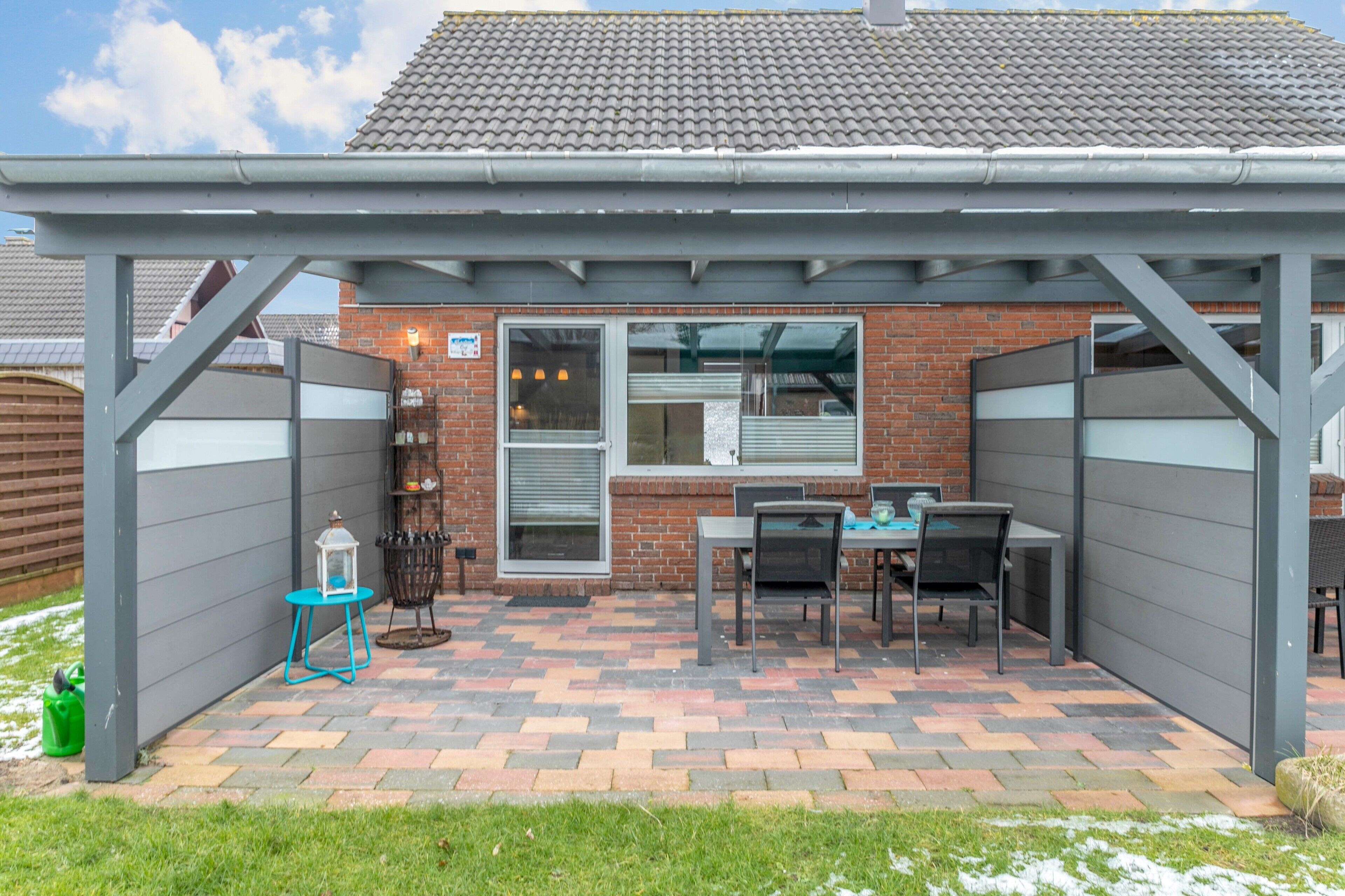 A covered patio area with a brick wall, a table and chairs, and a small garden.