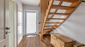 Una habitación con una escalera de madera, un aparador de madera y una puerta que da a otra estancia.