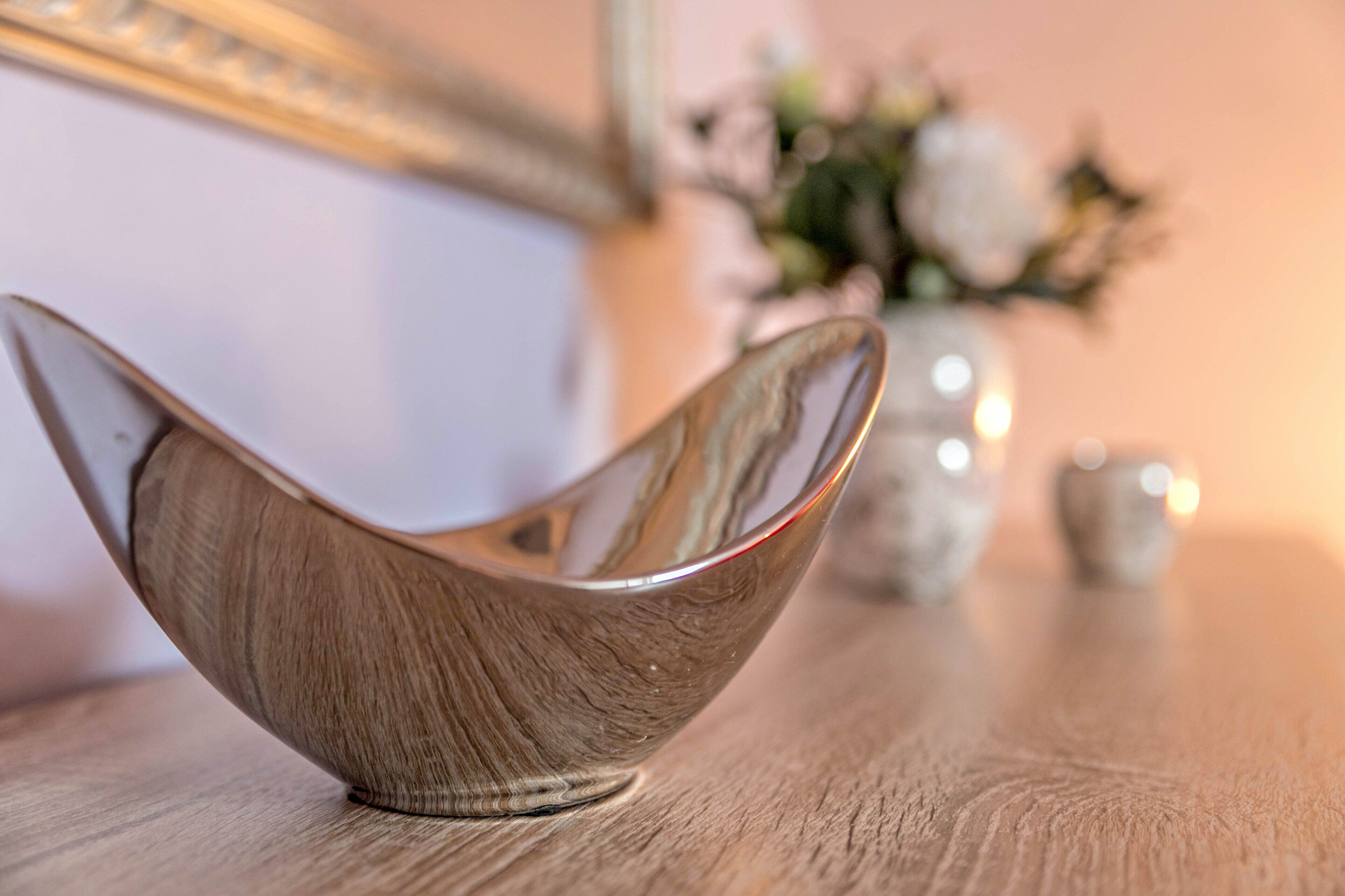 A wooden bowl on a table with a blurred vase and flowers in the background.