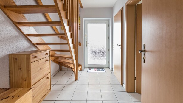 Una escalera de madera que lleva a una puerta, un armario de madera y un suelo de baldosas.