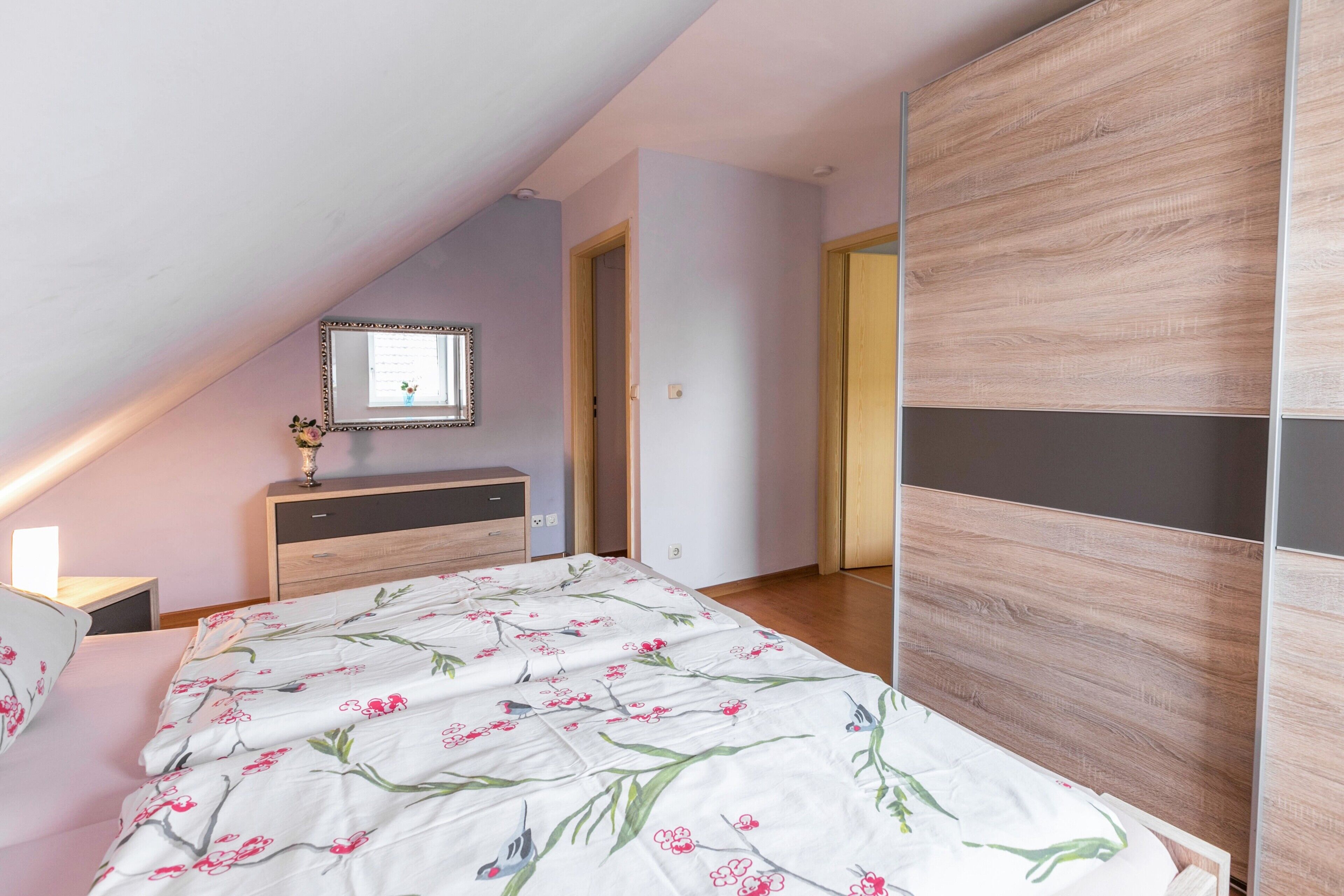 A bedroom with a bed, a dresser, a mirror, and a wardrobe.