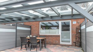 Un patio cubierto con un muro de ladrillo, una mesa con sillas y una ventana con persianas.