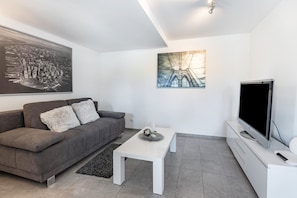A modern living room with a grey sofa, a white coffee table, a flat-screen TV, and two artworks on the walls.