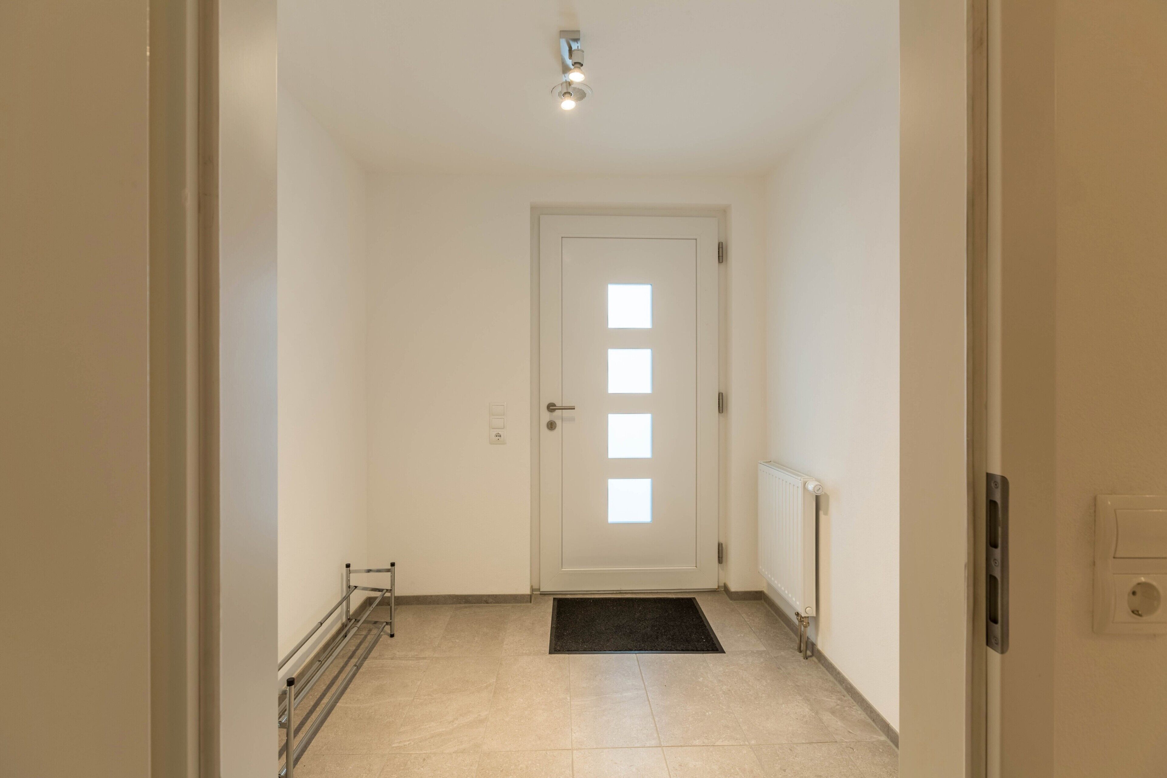 Un pasillo con una puerta blanca, un radiador y un felpudo negro.