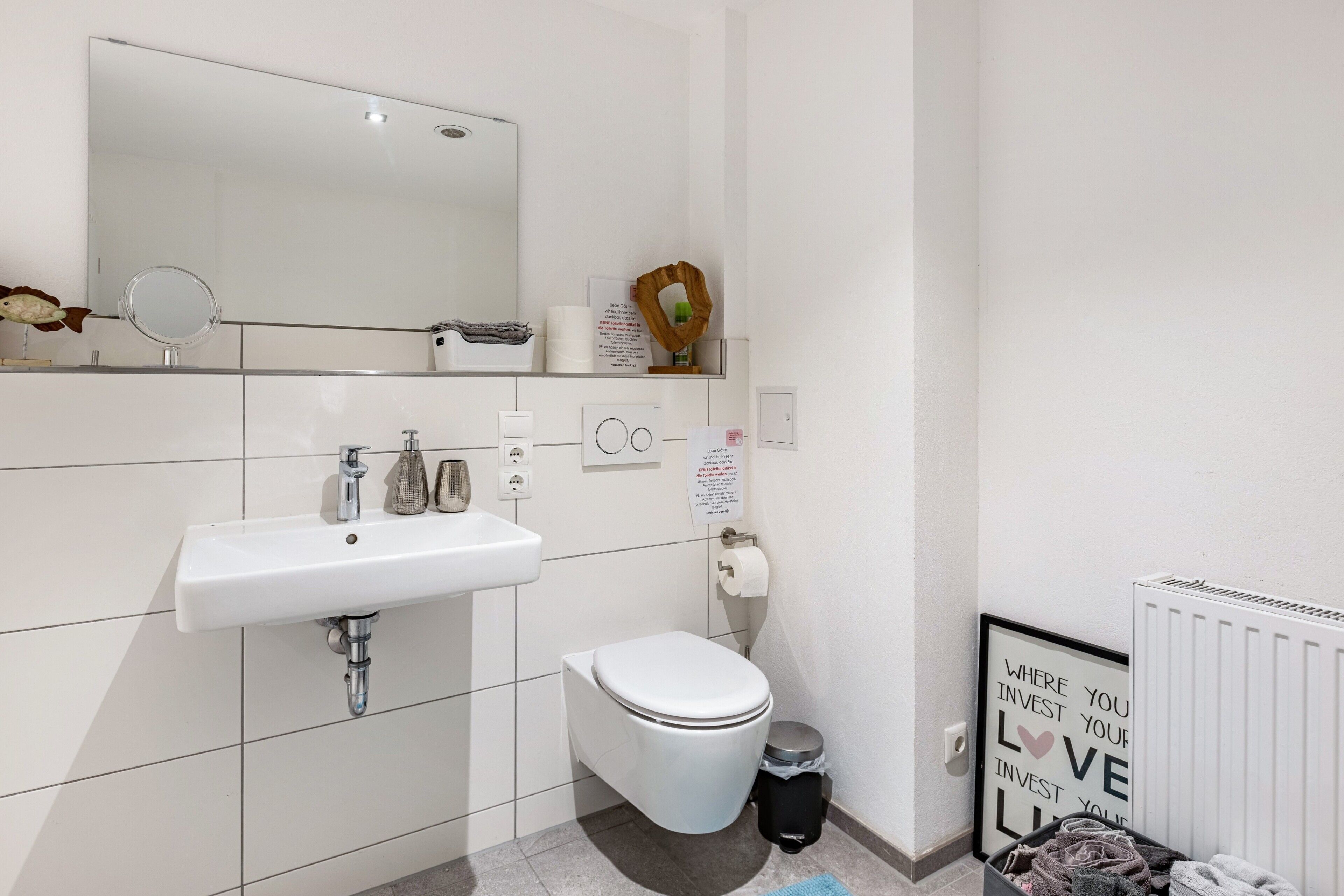 Une salle de bain moderne avec un lavabo blanc, un miroir, des toilettes et un radiateur.