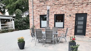 An outdoor seating area with a brick building, metal chairs, and potted plants.