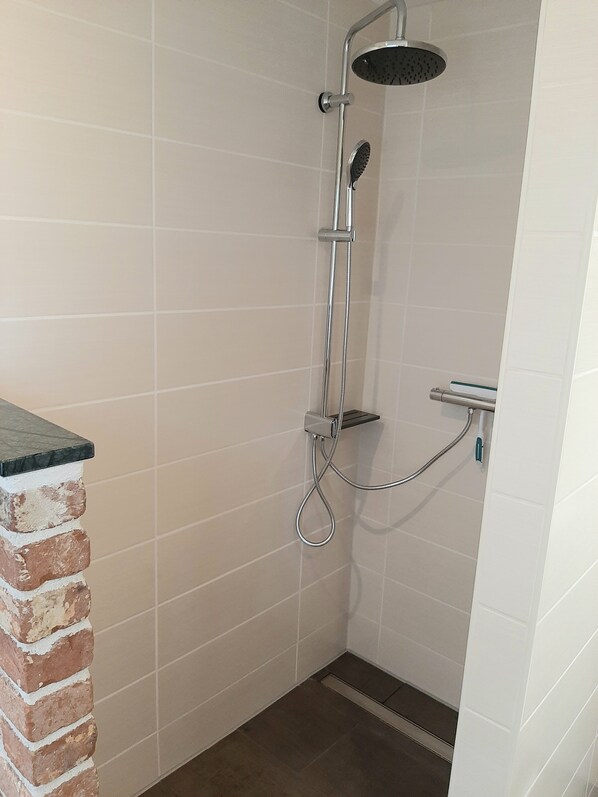 A shower area with a handheld showerhead, a wall-mounted showerhead, and a handheld showerhead with a hose.