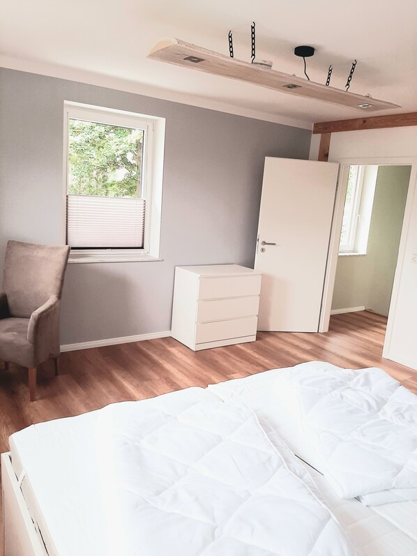 Un dormitorio con cama, una silla, cómoda y armario.