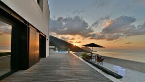 Een modern gebouw met een houten terras met uitzicht op een wateroppervlak bij zonsondergang.