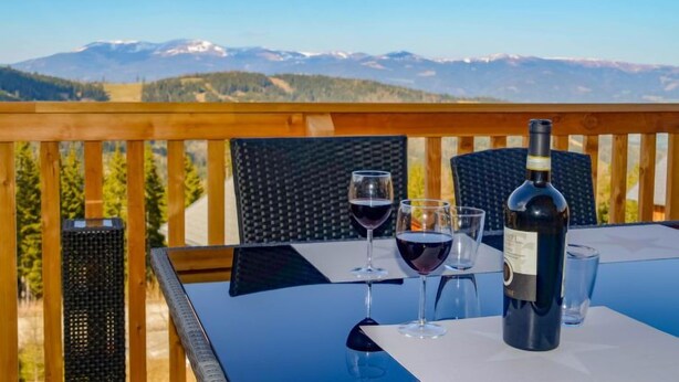 Une table avec une bouteille de vin et des verres, placée sur un balcon donnant sur un paysage montagneux.