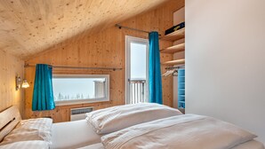 Une chambre confortable, aménagée dans une cabane en bois, avec deux lits, une fenêtre avec des rideaux et un placard intégré avec une tringle pour suspendre les vêtements.