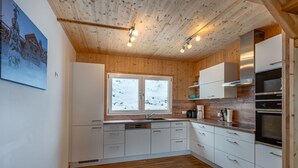 Une cuisine moderne avec un plafond et des murs en bois, des armoires blanches, une grande fenêtre donnant sur un paysage enneigé et des appareils électroménagers intégrés.