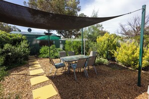A patio with a table and chairs, surrounded by mulch and plants.
