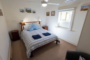 Ein Schlafzimmer mit Bett, Nachttischen, Deckenventilator, Fenster und Wandbildern.