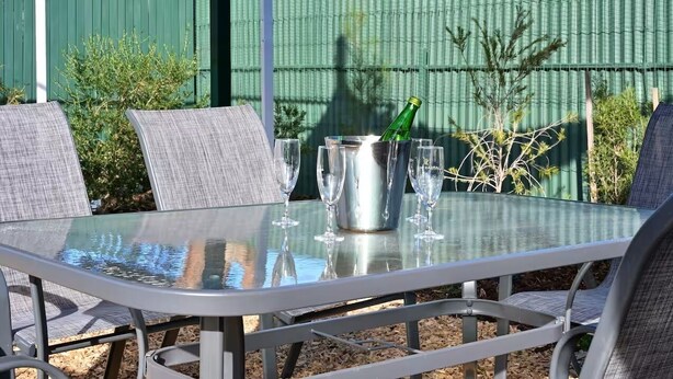 A glass-top table with metal chairs, a metal bucket with a bottle, and two glasses. - Hawker Bed and Breakfast (Hawker)