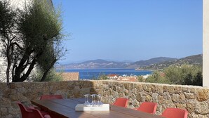 Un tavolo di legno con sedie rosse, una parete in pietra e vista sul mare e sulle montagne.