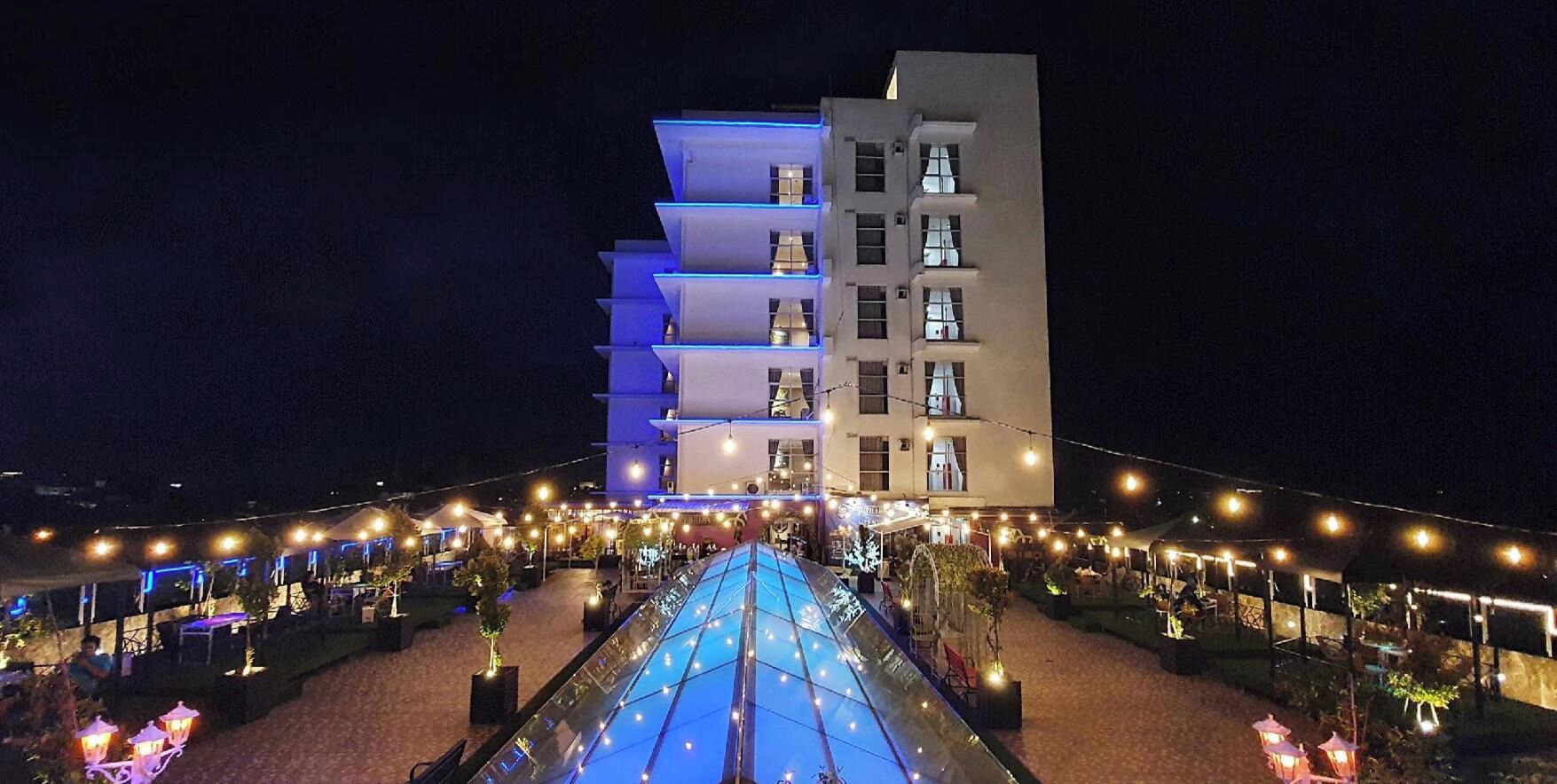 Un hôtel à plusieurs étages doté d’un espace extérieur couvert, agrémenté de guirlandes lumineuses et de sièges pour profiter de l’extérieur.