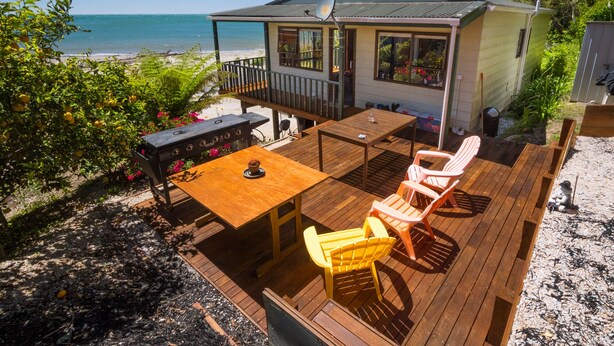 Eine Holzterrasse mit Tisch und Stühlen, mit Blick auf einen Strand.