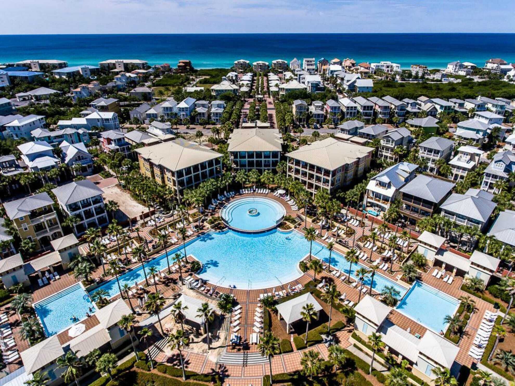 A resort with a central pool surrounded by villas and a view of the ocean.