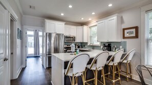 A modern kitchen with white cabinetry, stainless steel appliances, and a central island with bar stools.
