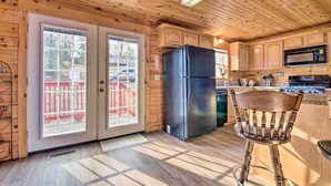 A wooden cabin kitchen with a black refrigerator, wooden cabinets, a microwave, and a dining area with a wooden chair.