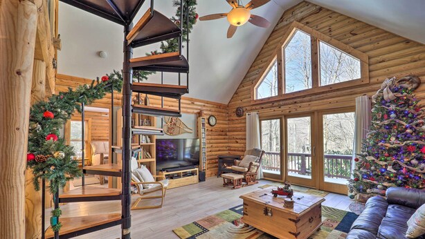 Een gezellig houten blokhut interieur met een houten trap, een open haard, een groot raam en een kerstboom.