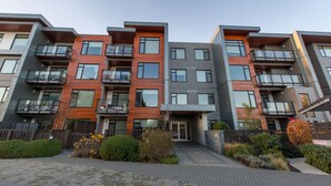 Un immeuble résidentiel à plusieurs étages, doté de balcons, d’une entrée sécurisée et d’un jardin paysager à l’avant.
