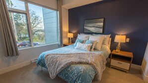 Une chambre à coucher avec un lit, deux tables de chevet, une fenêtre et un tableau accroché au mur.